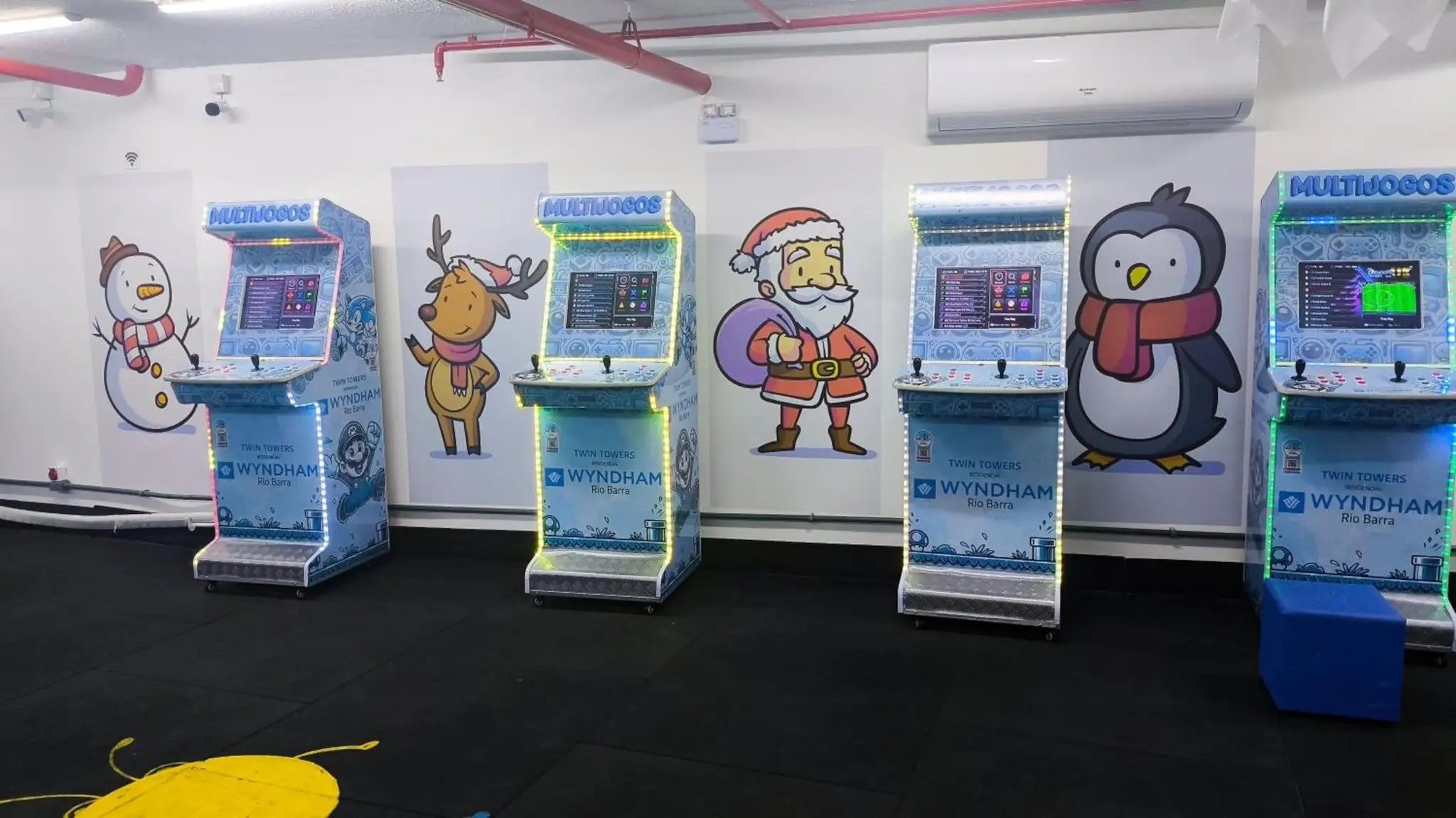 Una hilera de quioscos interactivos con personajes de caricatura, identificados con 'MULTIJOGOS' y 'WYNDHAM', en una habitación con piso negro y paredes blancas.