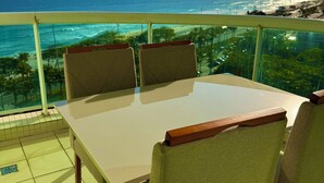 A dining area with a table and chairs, overlooking a beach and ocean. - Flat Beira Mar Barra da Tijuca Rio  (Rio de Janeiro)