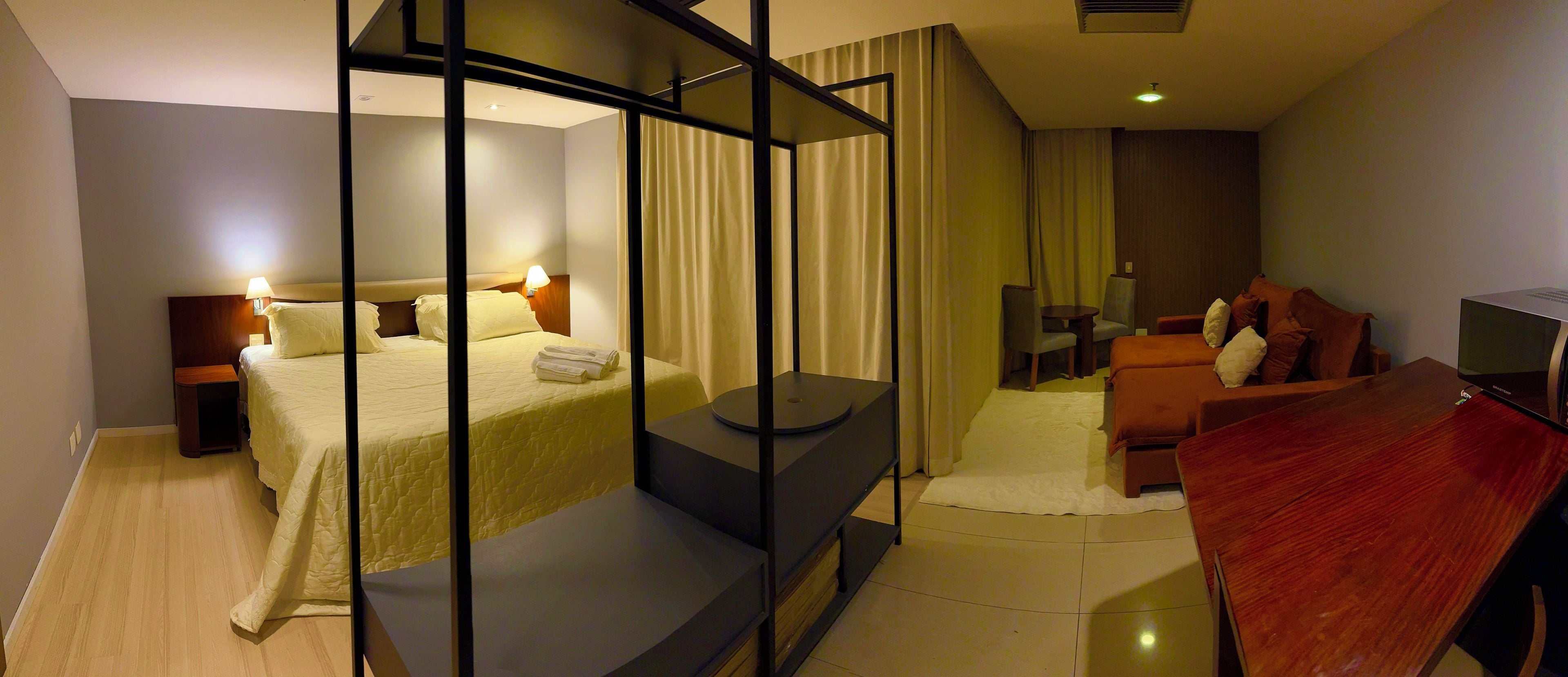 Quarto de hotel moderno com uma cama, área de estar, televisão e escrivaninha.