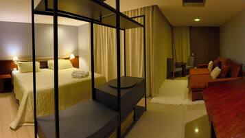 Quarto de hotel moderno com uma cama, área de estar, televisão e escrivaninha.