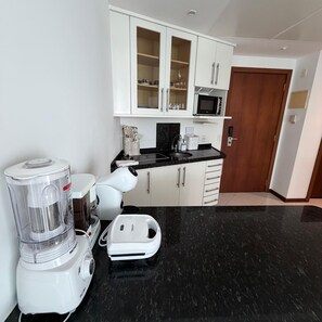 Una cocina moderna con gabinetes blancos, encimera negra, microondas y cafetera.