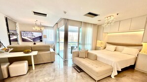 A modern hotel room with a large bed, a sofa, a desk, and a view of the city through large windows. - Flat Beira Mar Barra da Tijuca Rio  (Rio de Janeiro)