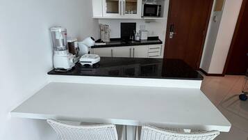 Cozinha moderna com armários brancos, bancada preta e duas cadeiras de vime.