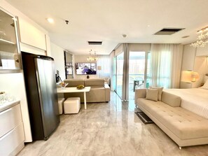 Una habitación de hotel moderna con kitchenette, un sofá, un comedor y un amplio ventanal con vista a la ciudad.