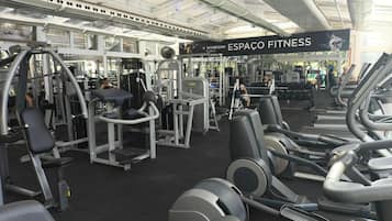 A gym with various exercise equipment, a banner reading 'WYNDHAM ESPAÇO FITNESS,' and a large window allowing natural light.