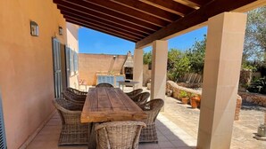 Eine Terrasse im Freien mit Holztisch, Korbstühlen, einem Grill und Blumentöpfen.