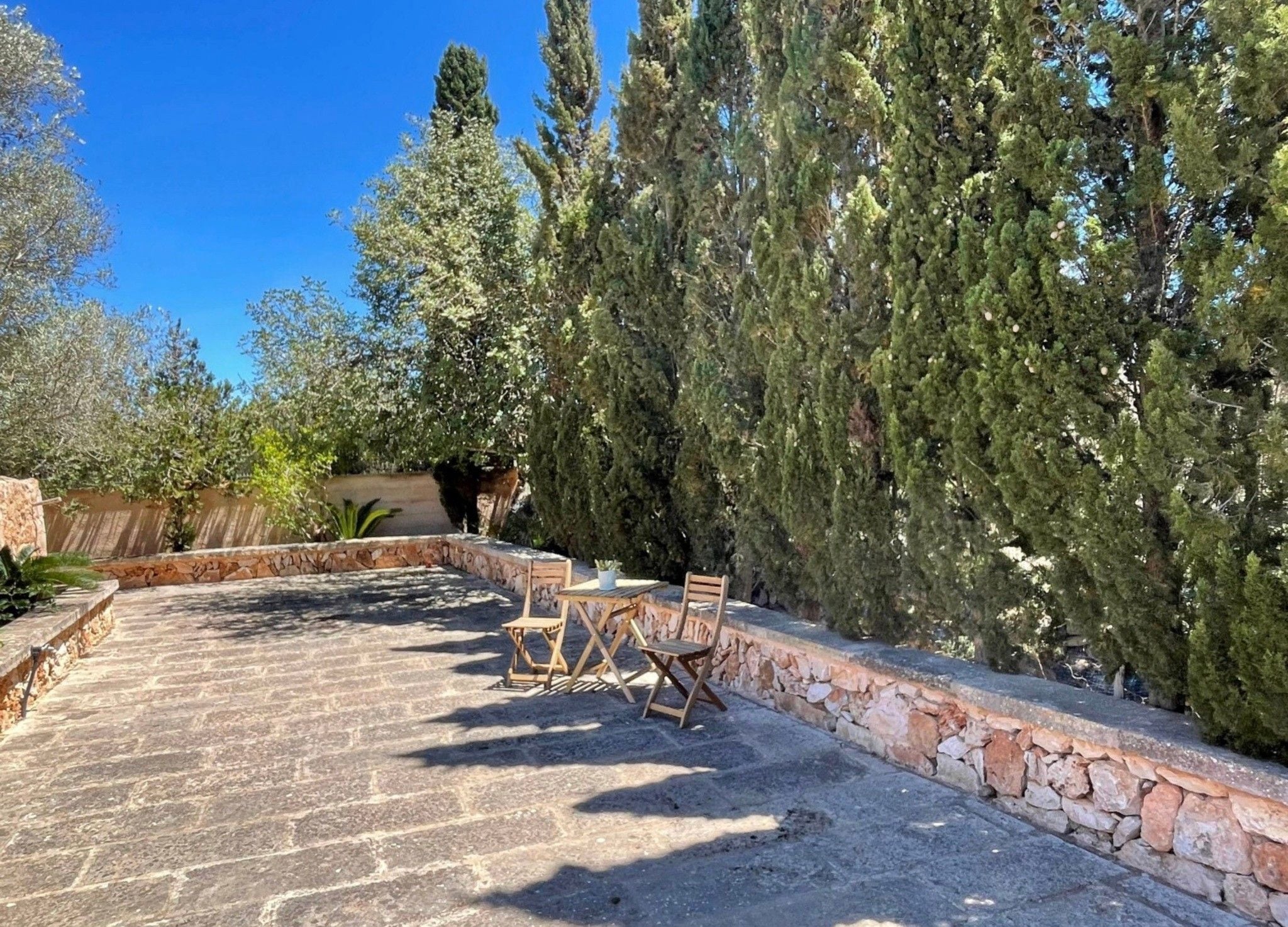 Un patio al aire libre con suelo de piedra, muebles de madera y una pared de piedra.