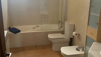 Une salle de bain avec une baignoire, deux toilettes, une douche et une fenêtre.