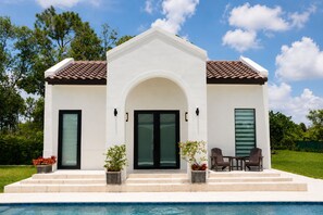 A modern house with a swimming pool, featuring a central archway, two doors, and a patio with outdoor furniture.