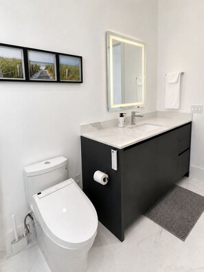 A modern bathroom with a toilet, bidet, sink, and mirror.