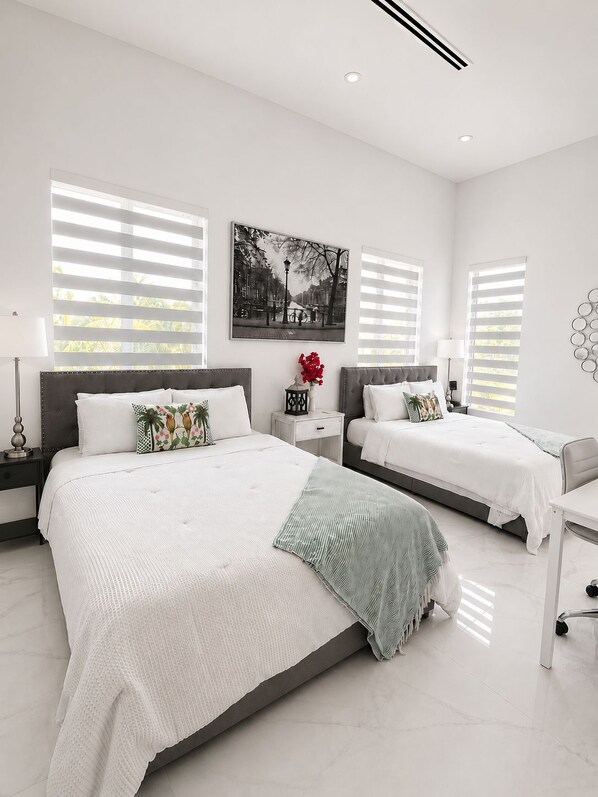 A modern bedroom with a large bed, two bedside tables, a desk, and a wall-mounted lamp.