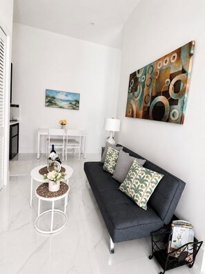 Un salon moderne avec un canapé gris, une table basse et deux petites tables d’appoint. Un tableau est accroché au mur et une lampe est posée sur le canapé.