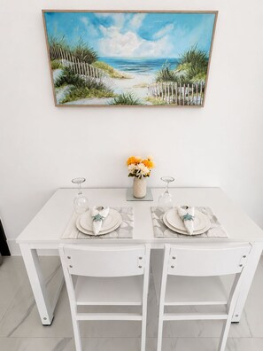 A dining table set for two with a beach painting above it.
