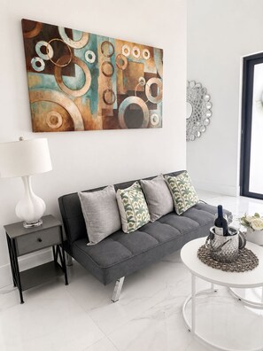 A modern living room with a grey sofa, a white side table, a round coffee table, and a large abstract painting on the wall.