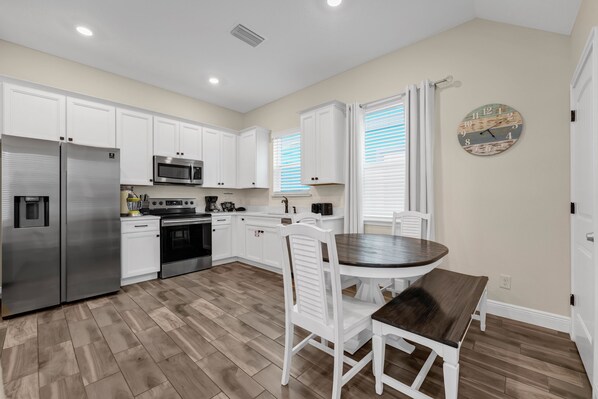 A modern kitchen with white cabinetry, stainless steel appliances, and a wooden dining table.