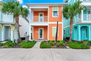 A row of colorful townhouses with a central entrance, each with a balcony and a small garden area.