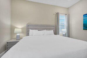 A hotel room with a large bed, two bedside tables, and a window with blinds.