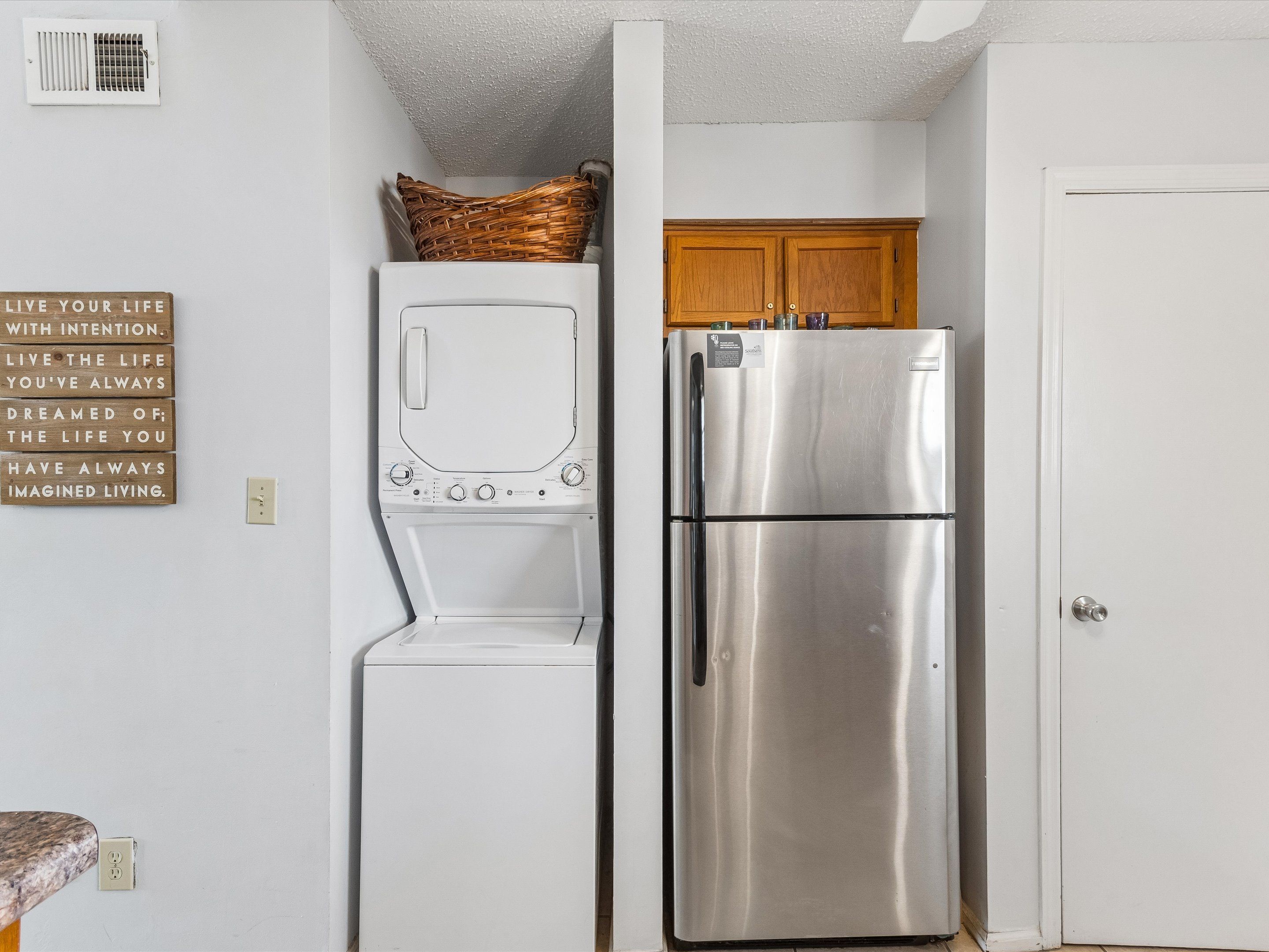 A compact kitchen with a stainless steel refrigerator, a built-in oven, and a wall-mounted basket.