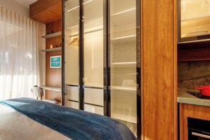 A bedroom with a bed, a wooden wardrobe, a shelf with decorative items, and a window with curtains. - Privilege Jardins - Elegance with parking included (São Paulo)