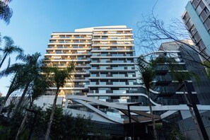Ein modernes, mehrstöckiges Gebäude mit einer gewölbten Fassade, umgeben von Palmen und anderer Vegetation.