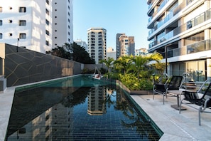 Ein Swimmingpool mit geometrischem Wanddesign, umgeben von Sitzgelegenheiten im Freien und Grünflächen.