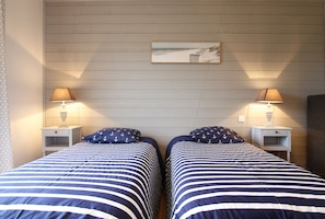 A double bed room with striped bedding, two bedside lamps, and a framed picture on the wall. - Cottage 'Utah Beach' with Private Terrace, Private Garden and Wi-Fi (Sainte-Marie-du-Mont)