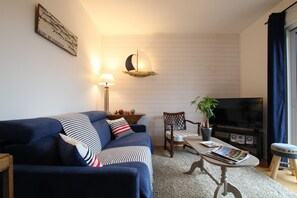 Ett vardagsrum med en soffa, en fåtölj, ett soffbord, en tv och en vägghylla med dekorativa föremål.