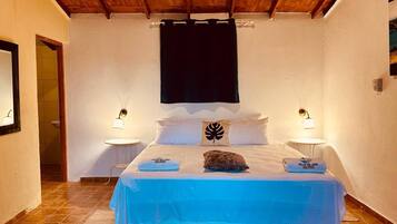 A bedroom with a bed, two bedside tables, a nightstand, a wooden ceiling, and a wall-mounted light fixture.