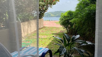 A view through a window with a table and chair, a potted plant, and a distant landscape with a body of water and hills.