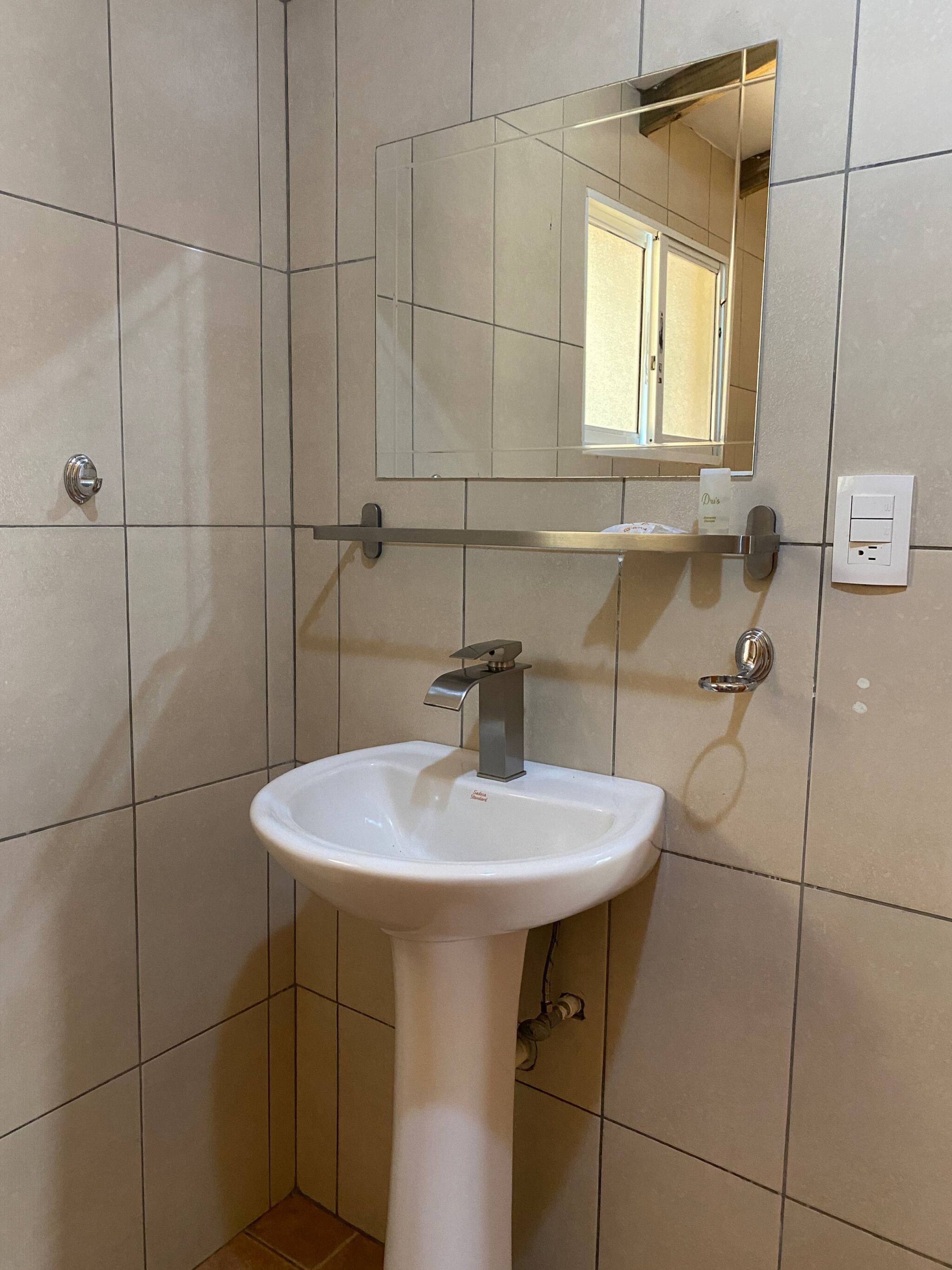 Een badkamer met een witte wastafel op een voetstuk, een spiegel erboven en een handdoekdispenser.