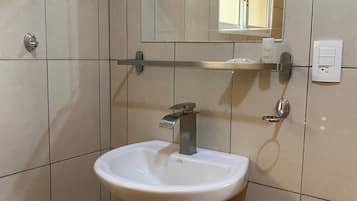 Een badkamer met een witte wastafel op een voetstuk, een spiegel erboven en een handdoekdispenser.