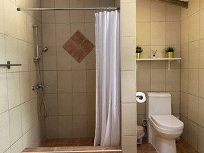 Ein Badezimmer mit Dusche, Toilette und einem Regal mit Pflanzen.
