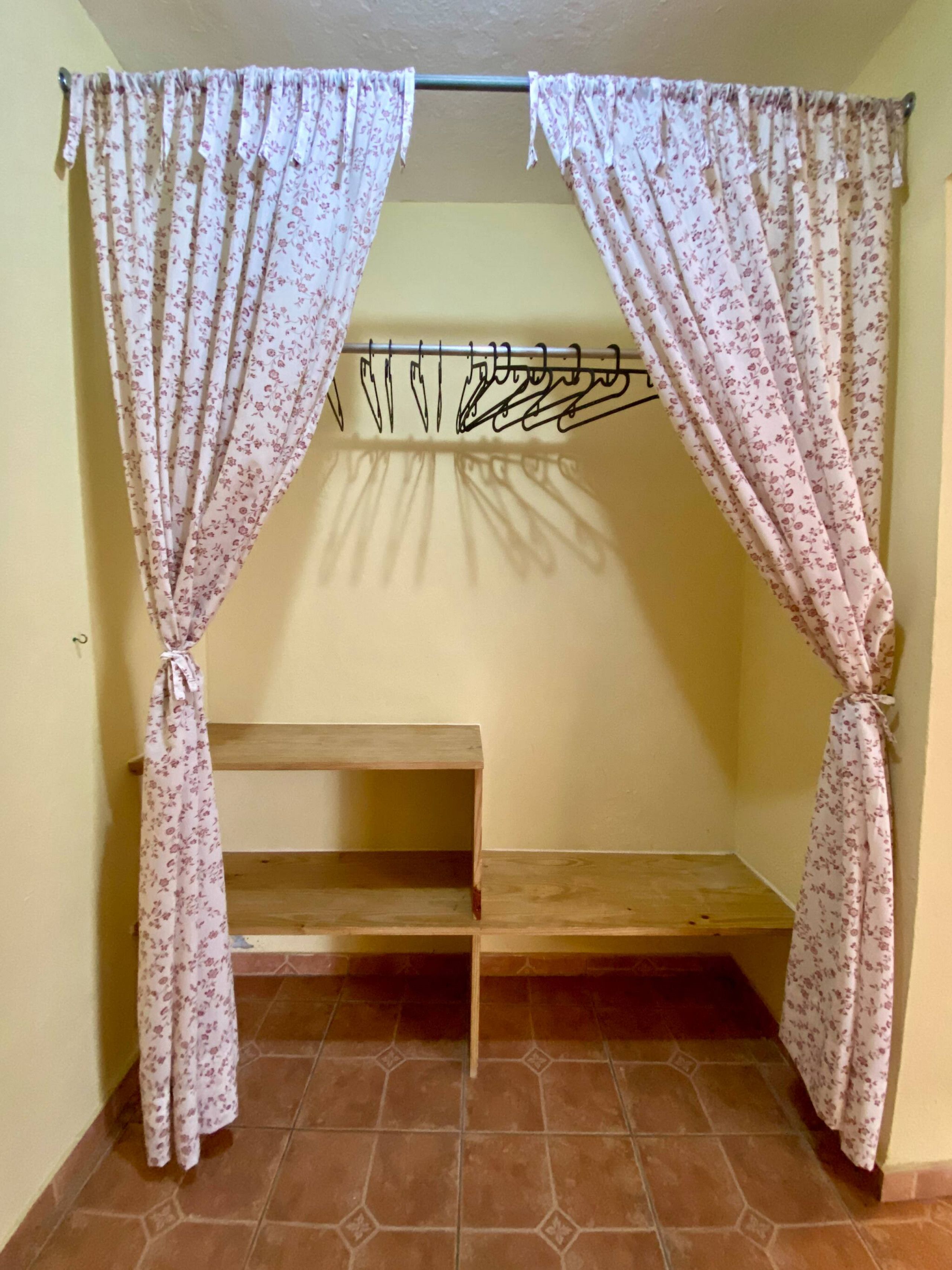 A room with a wooden bench, floral curtains, and a metal rack against the wall.