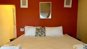 A hotel room with a bed, pillows, a nightstand, a lamp, and a mirror on the wall.