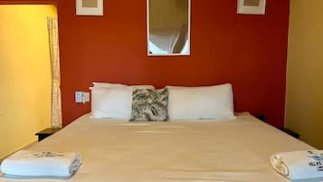 A hotel room with a bed, pillows, a nightstand, a lamp, and a mirror on the wall.