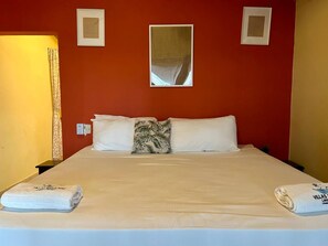 A hotel room with a bed, pillows, a nightstand, a lamp, and a mirror on the wall.