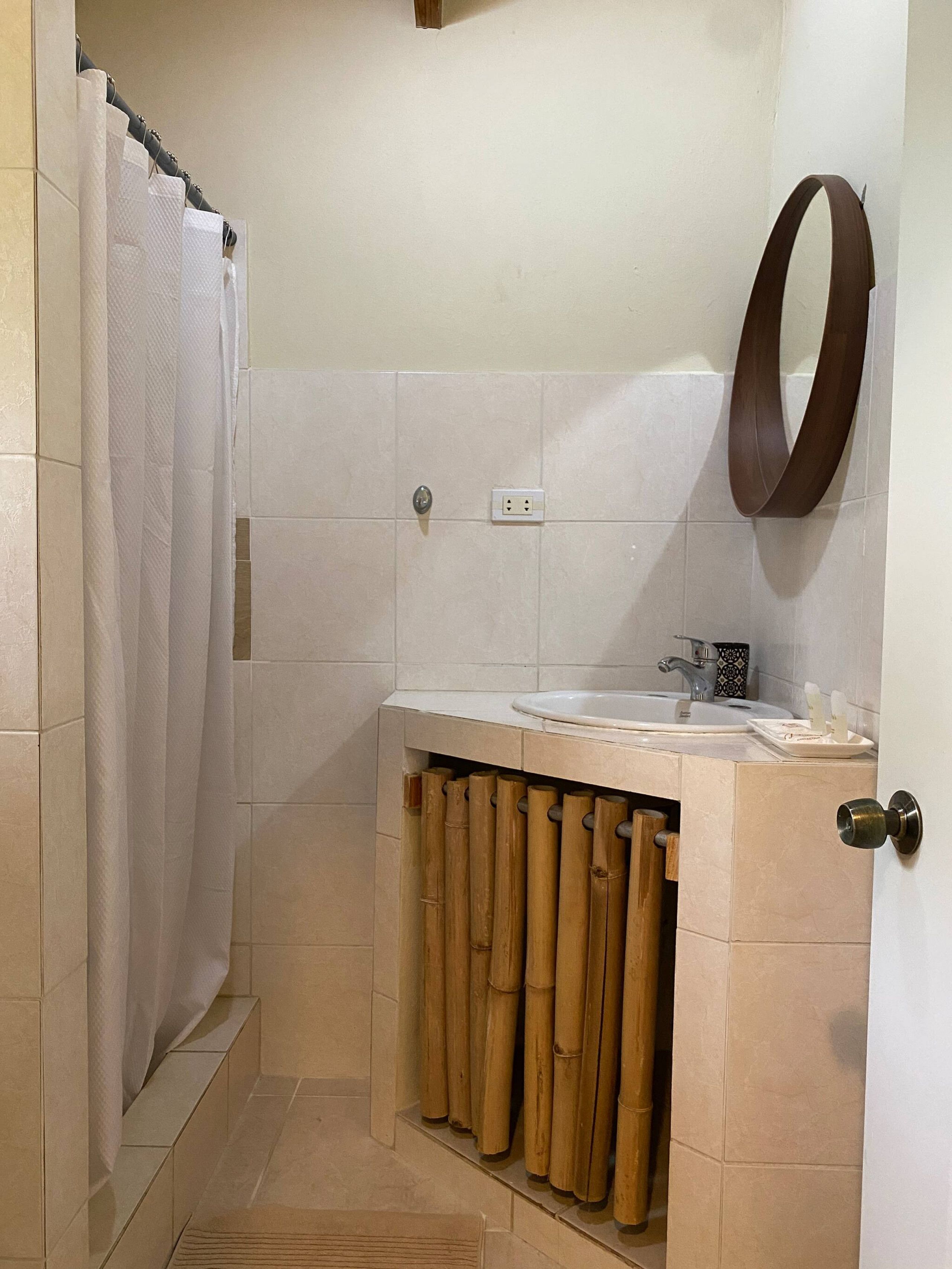 Un baño con cortina de ducha, un lavamanos, un espejo y un perchero para toallas.