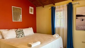 A hotel room with a bed, a window with curtains, and a poster on the wall.