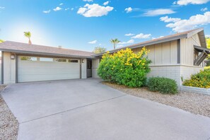 A residential house with a garage, a driveway, and a well-maintained garden with yellow flowering plants. - Paradise Palms - Scottsdale 4BR w/ Heated Pool, Fire Pit, PingPong (Scottsdale)