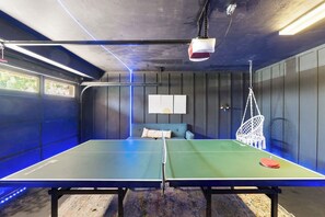 Une table de ping-pong avec un filet, un fauteuil suspendu et un projecteur fixé au mur, dans une pièce aux murs lambrés et dotée d’un mur d’accent bleu.
