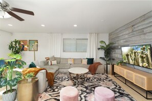 A modern living room with a sectional sofa, a coffee table, a TV, and decorative plants. - Paradise Palms - Scottsdale 4BR w/ Heated Pool, Fire Pit, PingPong (Scottsdale)