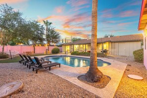 A swimming pool with lounge chairs, a palm tree, and a building with a garage in the background. - Paradise Palms - Scottsdale 4BR w/ Heated Pool, Fire Pit, PingPong (Scottsdale)