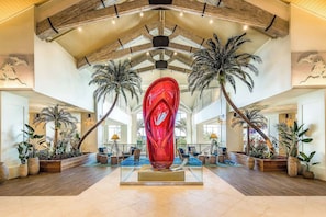 A spacious lobby with a central red sculpture, wooden ceiling beams, and multiple palm trees. - Palm Paradise Cottage near Disney | Private Pool & Resort Access - 8017ST (Kissimmee)