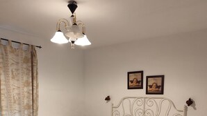Et soveværelse med seng, et natbord, et bord, mønstrede gardiner og en loftlampe.