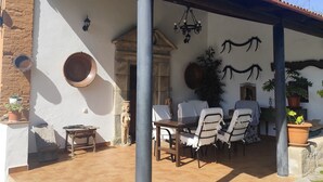 En overdækket terrasse med et bord, stole, en statue og en potteplante.