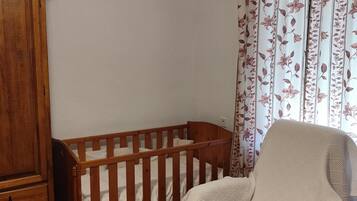Una habitación con una cuna de madera, una silla con funda blanca y cortinas estampadas.