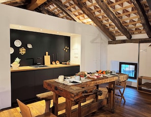 A rustic kitchen with a wooden table set for dining, a black backsplash, and a sloped ceiling with exposed beams.