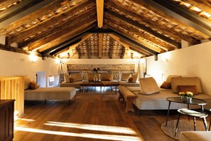 Un loft espacioso con vigas de madera a la vista, una pared de piedra y una zona de estar acogedora con sofás y una mesa de centro.
