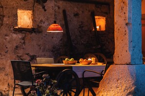 A rustic outdoor dining area with a table, chairs, and a bowl of fruit.