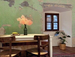 A room with a rustic wooden table, a vase with flowers, a window with wooden shutters, and a potted plant.